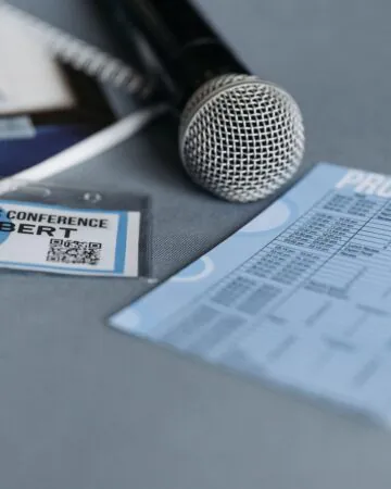 A microphone, name badge, program schedule, and notebook are placed on a grey surface at a business conference.