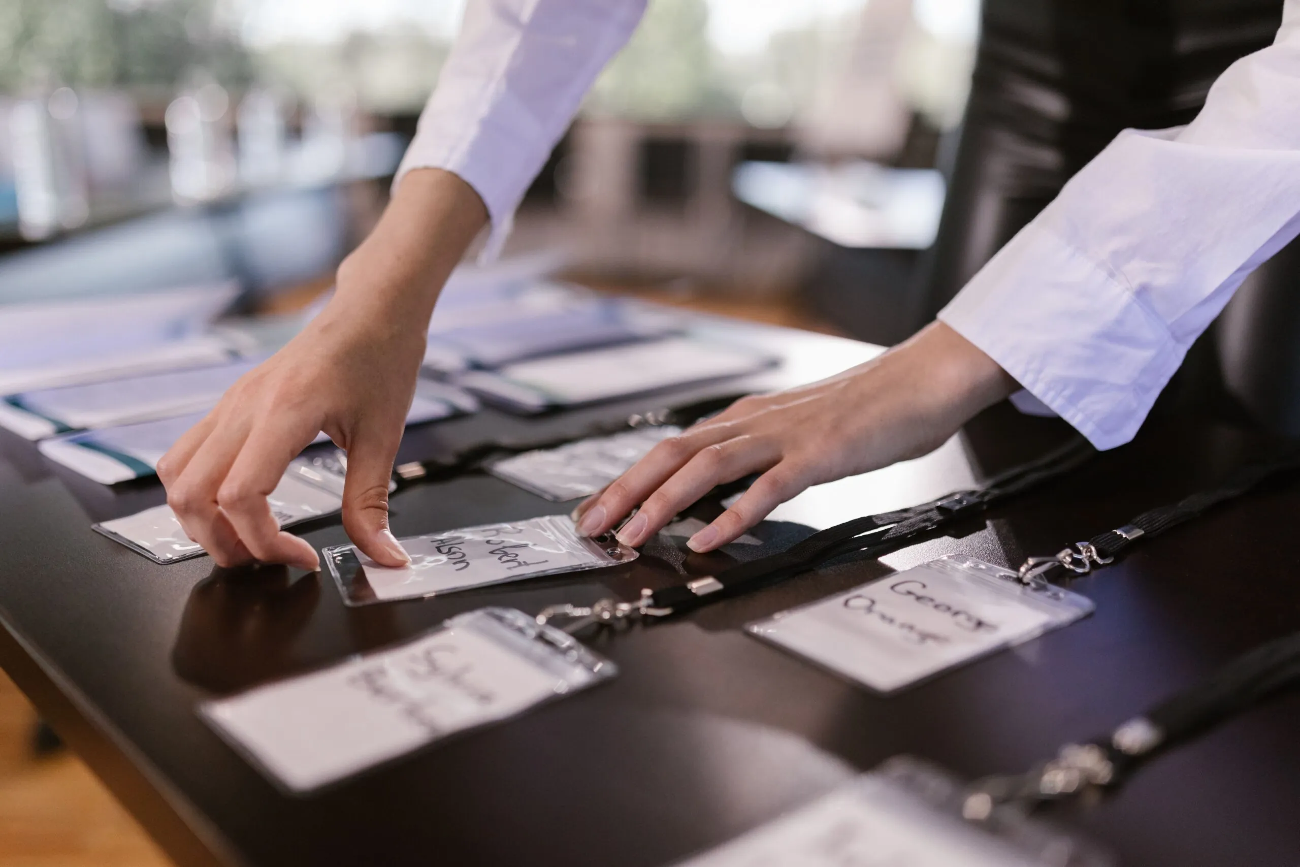 Person in a white shirt arranging name badges on a table for an event or conference, with more badges and papers in the background.